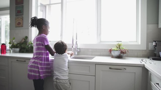 Older sister helping toddler brother wash hands at kitchen sink