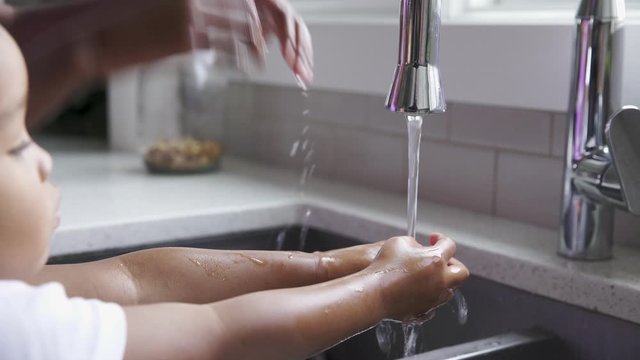 Sister helping toddler brother wash hands at kitchen sink