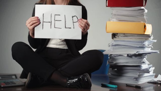 Close-up of tired and overloaded financial manager sitting on the desk near stack of unfilled documents and begging for help. Disappointed woman looking for help, financial calculations and data