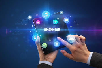 Businessman holding a foldable smartphone with #HASHTAG inscription, social media concept