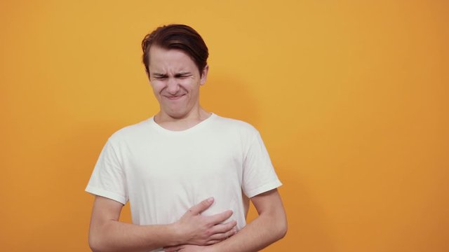 Stomach pains stomach problems white T-shirt young male on yellow background