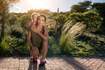 Beautiful mother and her little daughter outdoors. Beauty Mum and her Child sitting on Park pathway together at sunset. Outdoor Portrait of happy family. Mother's Day