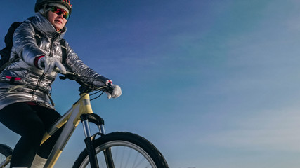 Woman is riding bicycle on the ice. Girl is dressed in a silvery down jacket, cycling backpack and helmet. Ice of the frozen Lake Baikal. Tires on bike are covered with spikes. Traveler is ride cycle.