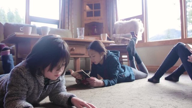 Brother and sister relaxing, reading books on cabin living room floor