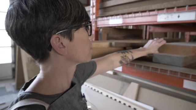 Woman Blowing Dust Off Wood From Storage In Community Workshop