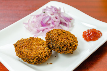 Crispy Beef Cutlets in a white plate along with onion salad and ketchup