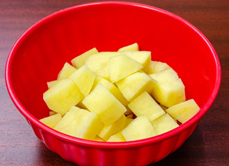 Beautifully cut potato cubes in a red bowl, ready to be cooked.