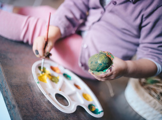 A child painting eggs for Easter, focus on hands, eggs, brush, and palette.