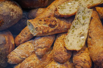Close up view, cutting heap and stack of HELLAS-STANGE, wheat bread mixed with feta cheese, olive and paprika, and various type of rustic and crusty wheat breads at display of bakery store. 