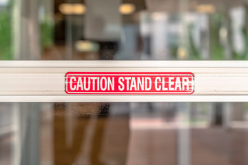 Caution Stand Clear sign on the metal plate of the glass door of a building