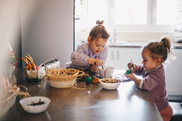 Two female toddlers painting eggs for easter in the living room.