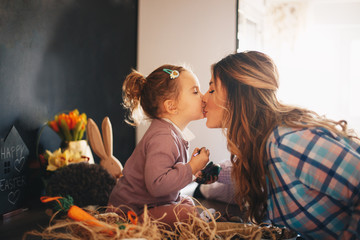 A mother and her toddler kissing affectionately in a living room filled with Easter themed...
