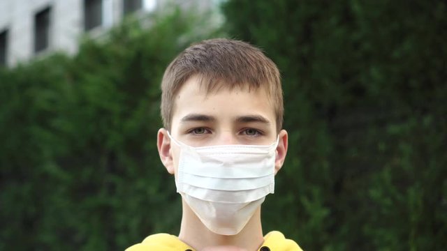 Sad young man teenager puts on a protective medical blue mask on a background of green vegetation. The idea of personal protective equipment against coronavirus and plant pollen for allergies