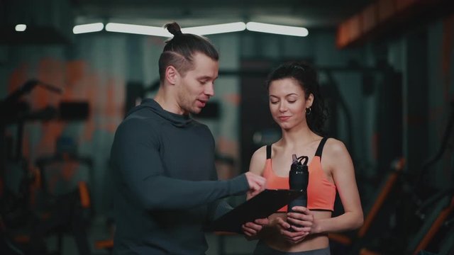 personal trainer with clipboard talking with sporty woman in gym