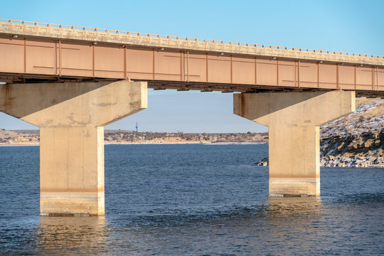 Focus on a beam bridge supported by abutments over blue lake against cloudy sky