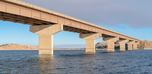 Stringer bridge spanning over a lake with view of snowy terrain and cloudy sky