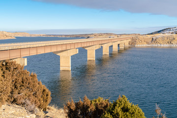 Blue lake with bridge connecting vast terrains blanketed with snow in winter