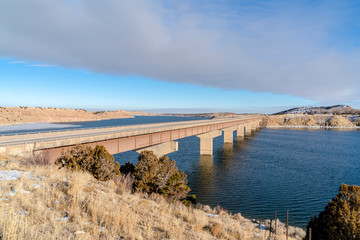 Obraz premium Bridge over lake connecting hills covered with snow on a sunny winter day