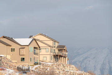 Homes on a hill with snowy roofs and yards against mountain and sky background