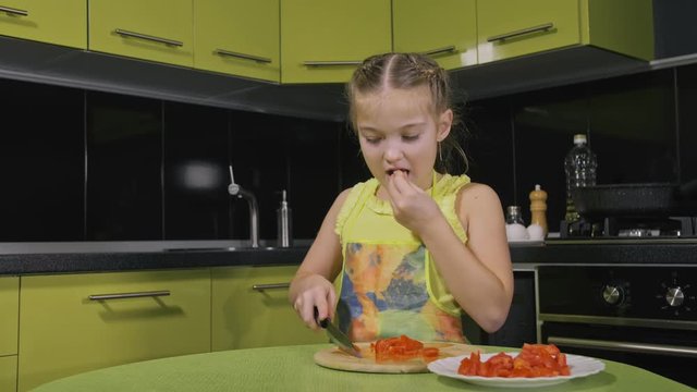 Smart girl learning to cook. Happy and serious young mistress children to cook a Neapolitan egg fried omelette from sausage. Modern Built In Kitchen Appliances in green black color. Cut tomato dill.