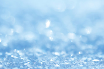 Snow crystals. Festive Christmas glare and sparkling blue background with natural snowflakes. Real snowy surface in the open air. Winter background.