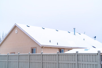 Home exterior with gable roof blanketed with snow against cloudy sky in winter