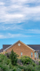 Vertical frame Blue sky and clouds over a home with gray roof and brick exterior wall
