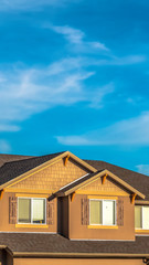 Vertical House exterior with dormers and gray roof against hills and cloudy blue sky