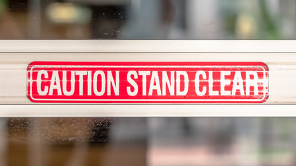 Panorama Caution Stand Clear sign on the metal plate of the glass door of a building