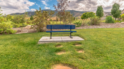Panorama Blue metal bench on vast grassy field with scenic mountain and cloudy sky view