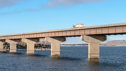Panorama Truck travelling on a beam bridge over lake against rugged land and cloudy sky