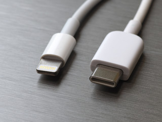 USB type C and lightning white cable connector on a gray metal background