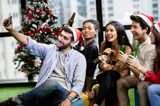 Ethnically diverse group office staff are celebrating Christmas in their office. They're taking selfie fun and happy.
