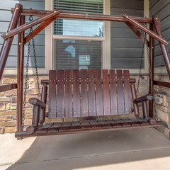 Square Brown wooden bench swing at the porch of a home with pastel blue front door
