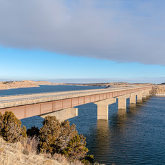 Fototapeta premium Square frame Bridge over lake connecting hills covered with snow on a sunny winter day