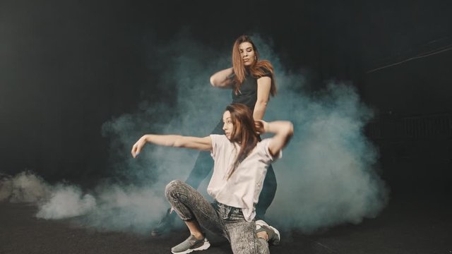 Two young women training their styles of dancing in the smoky studio
