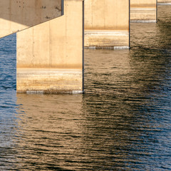Square Views underneath a beam bridge with abutments against the sunlit lake water