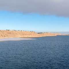 Square Scenic view of blue lake with frozen water near the base of a slope in winter