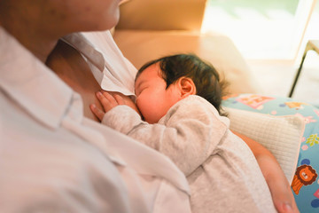 Breast feeding from mother to her baby. Newborn baby is hold by his mother while breast feeding.