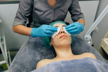 Doctor beautician removes a cosmetic mask with napkins from the patient's eye, beauty procedure