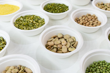 Peeled beans in a white plastic plate. Around in the same plates are various seeds, nuts and beans.
