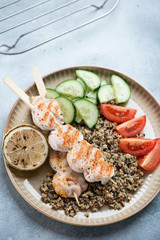 Roasted chicken skewers with quinoa and fresh vegetables on a round beige plate, studio shot over light-blue stone background