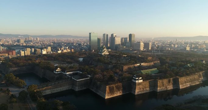 Slow flying towards Osaka castle buildings in public park at sunrise.