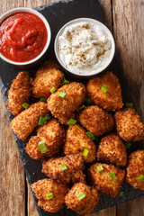 Coconut crispy chicken with two sauces close-up on a slate board. Vertical top view