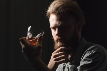Portrait of a pensive handsome young man, with a glass of alcohol in his hands.