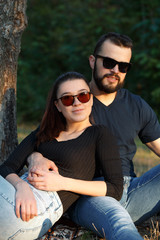 Portrait of a man and a woman in sunglasses in the woods. Young stylish couple on the background of nature. Warm autumn evening in the forest.
