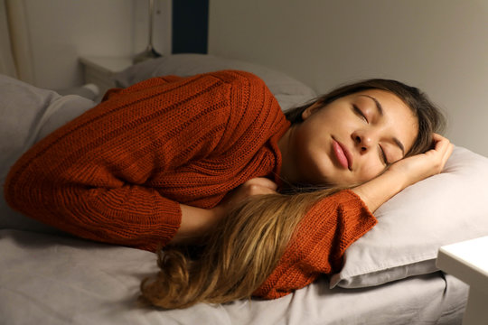 Relaxed young woman sleeping on bed at night