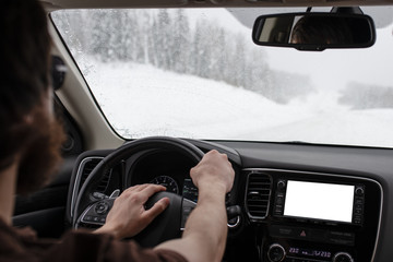 Man holding steering wheel while driving his car on a winter mountain road in blizzard.  Press on air horn to make a beep. Free copyspace on car tablet screen. Navigation system concept.