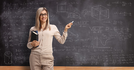 Female teacher holding a chalk in front of a school blackboard