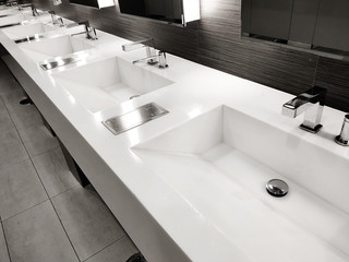 Public empty restroom with washstands, baby changer, and toillets in mirror. White sink row with mirrors and lights. Top horizontal view copyspace